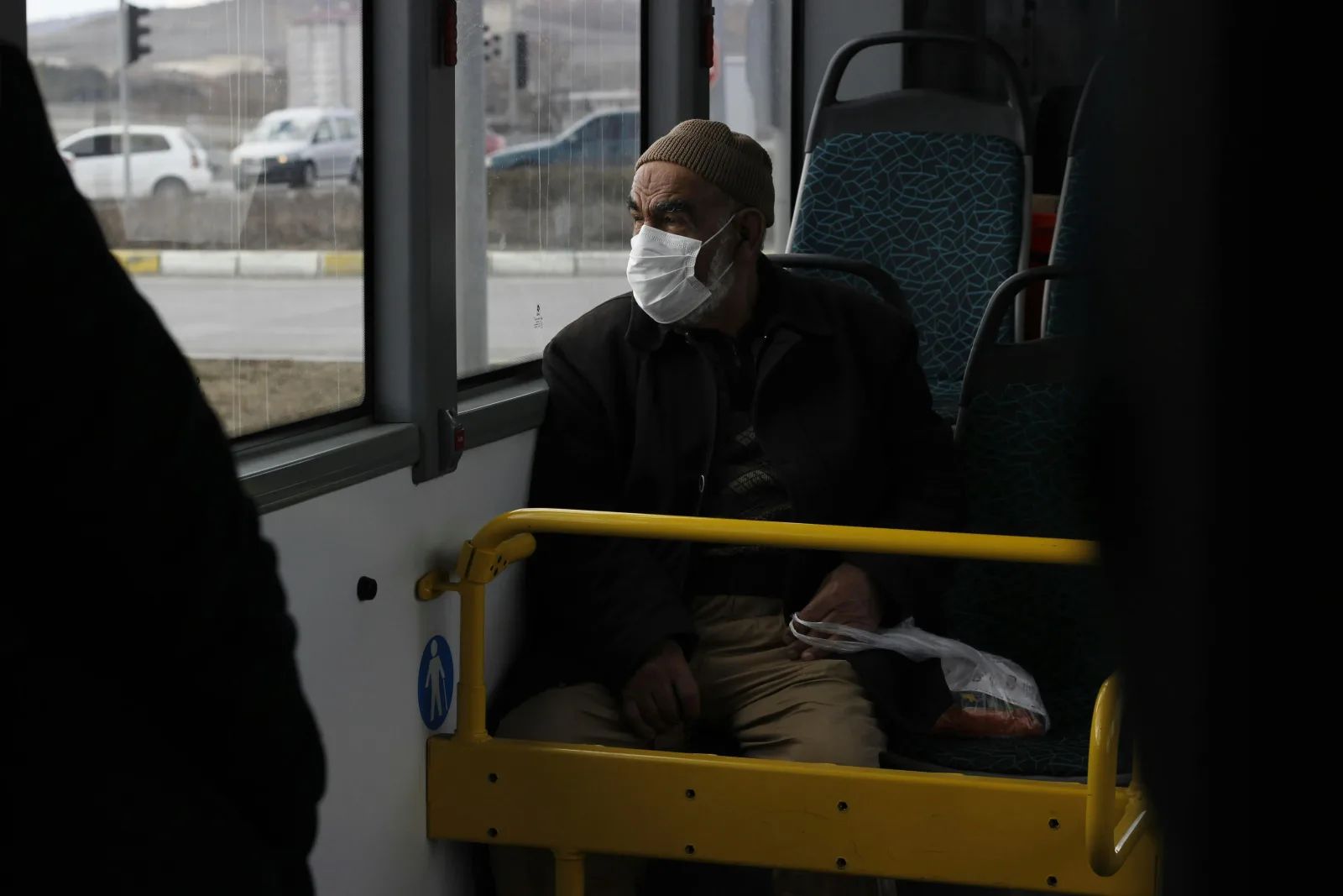 Un homme âgé, bonnet sur la tête et masque sur le visage, assis dans un bus, regarde par la fenêtre.