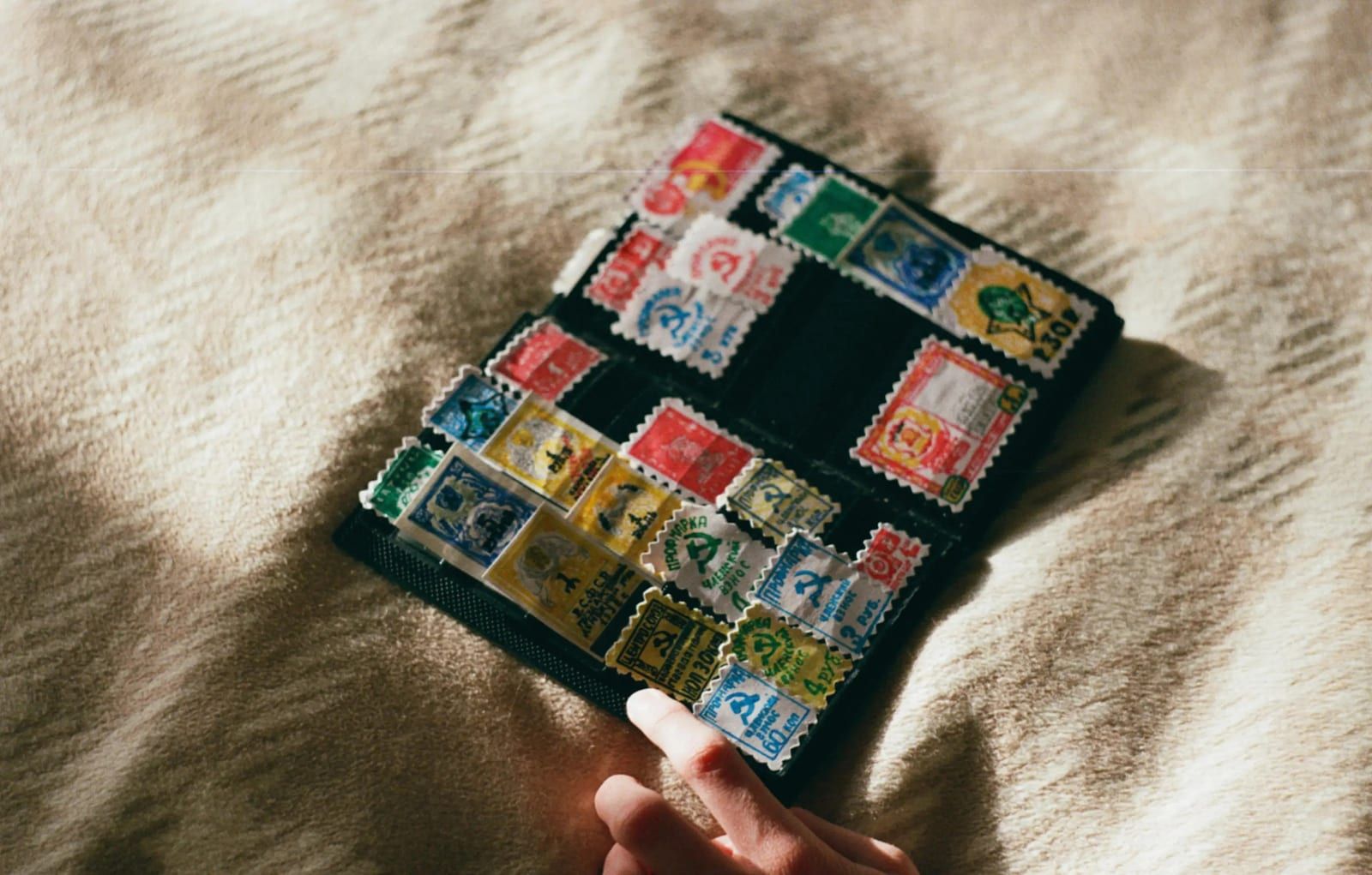Un classeur ouvert rempli de timbres colorés, posé sur une couverture en laine.