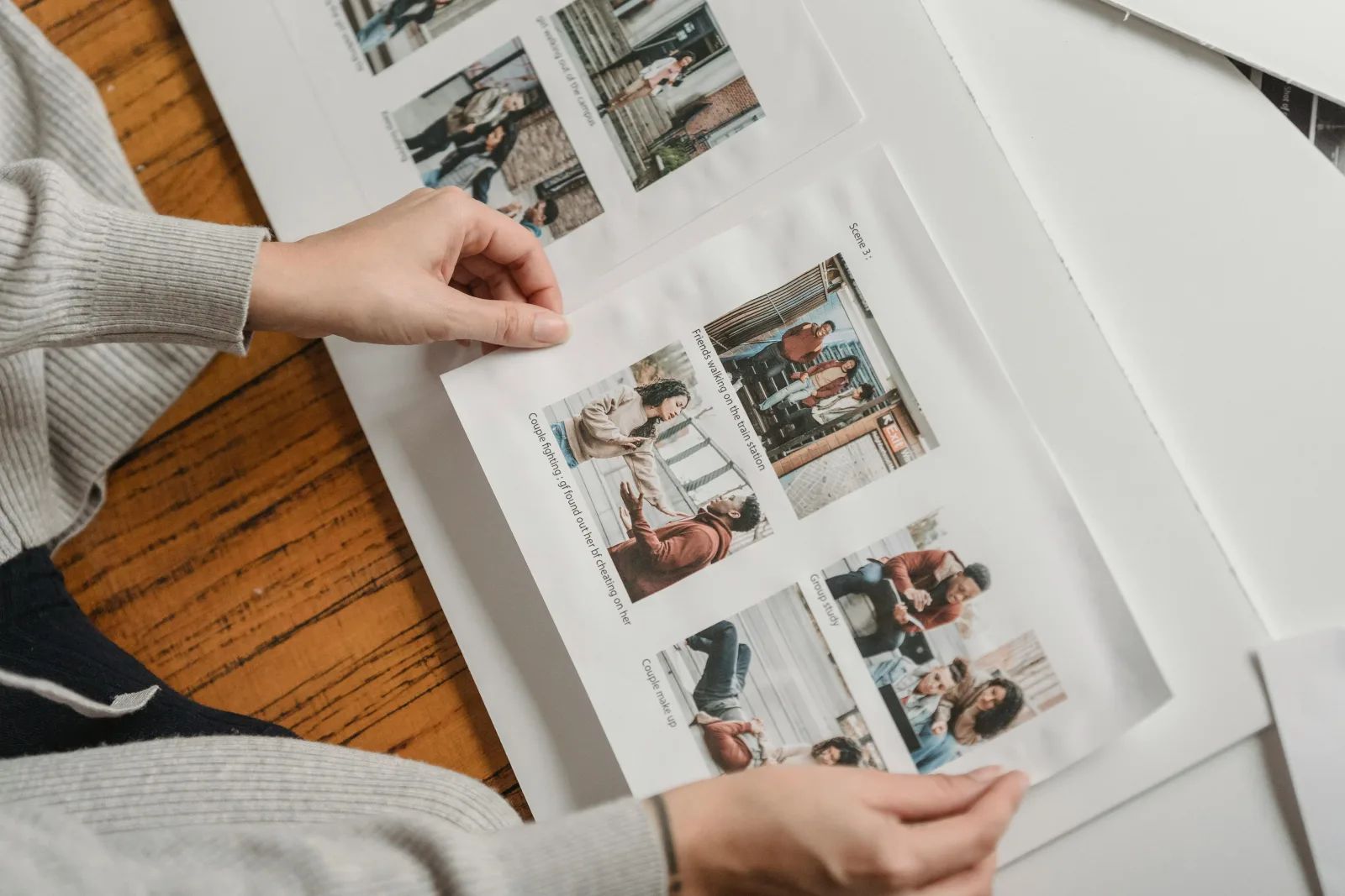 Deux mains feuillettent les pages imprimées d’un album de photos, posé sur une table en bois.