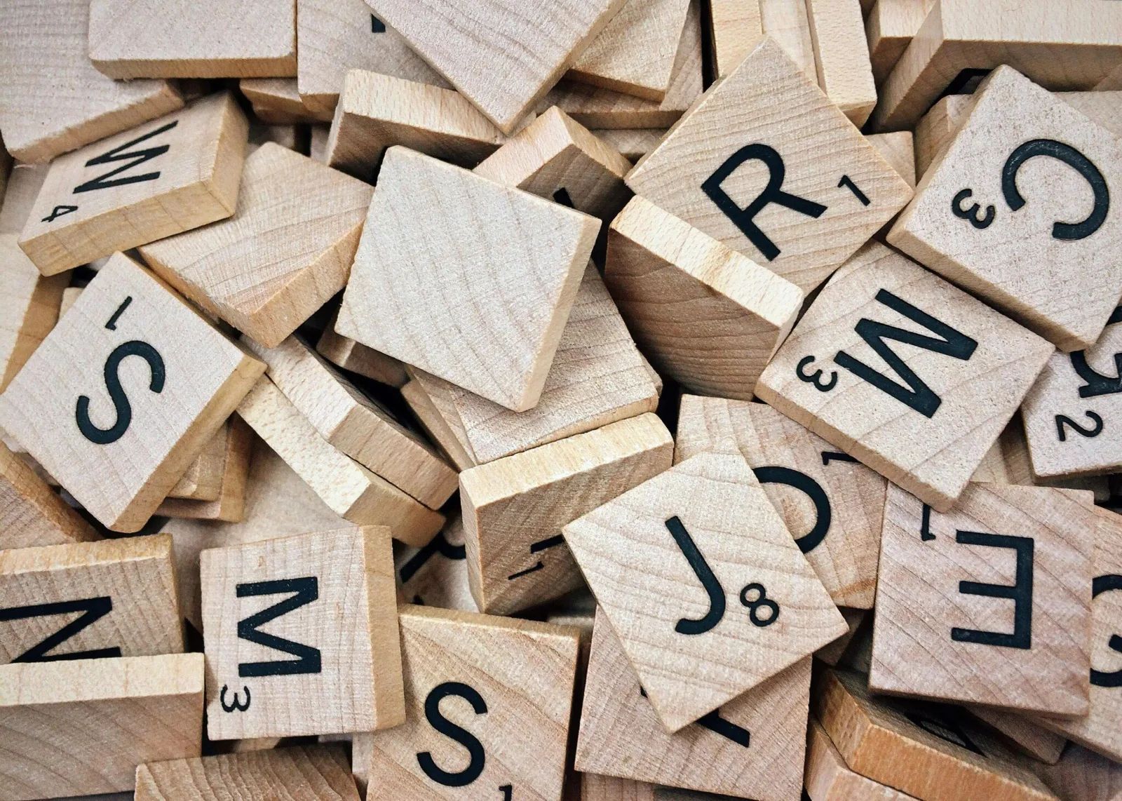 Des lettres de Scrabble en bois, posées en vrac les unes sur les autres.