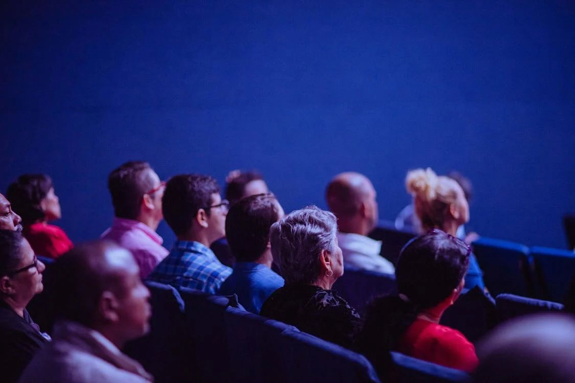 Des spectateurs de tous âges, assis dans les fauteuils bleus d’une salle de cinéma.