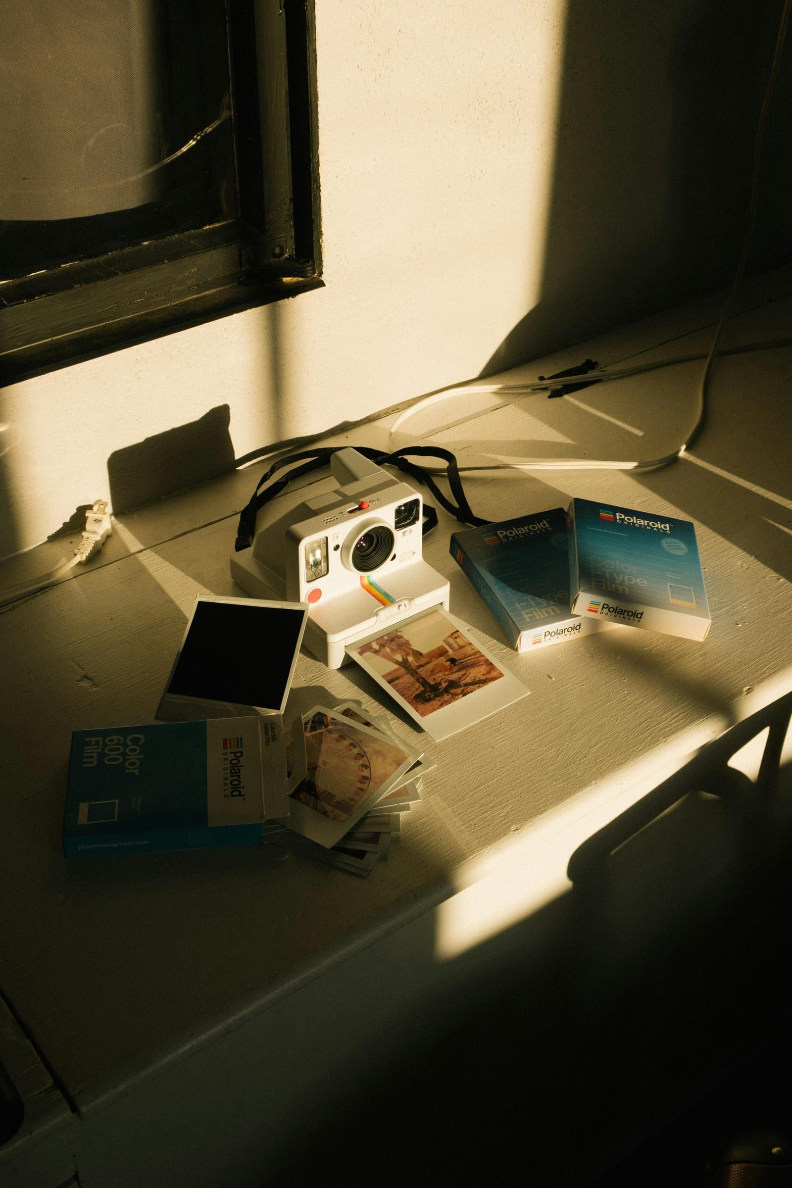 Un appareil photo instantané blanc posé sur une table, entouré de photos et de boîtes de pellicule.