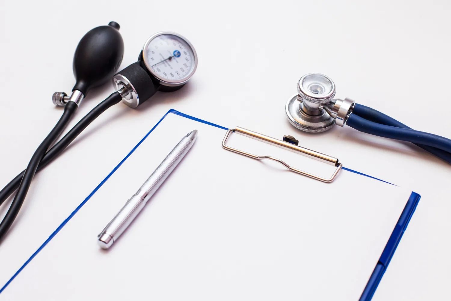 Un porte-bloc vierge et un stylo posés sur une table, entre un tensiomètre et un stéthoscope.