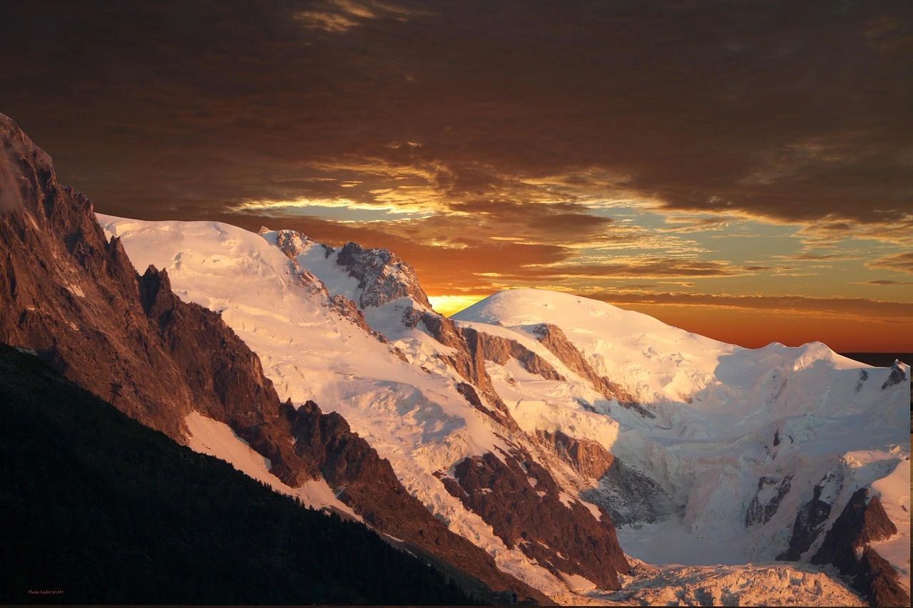 Le massif enneigé du Mont-Blanc éclairé par le soleil couchant, sous un ciel orangé.