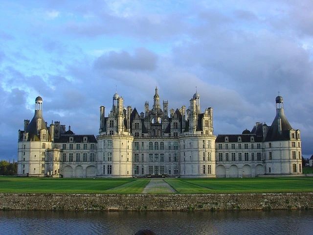 Le château de Chambord et ses tours, au bord de l’eau, sous un ciel nuageux.