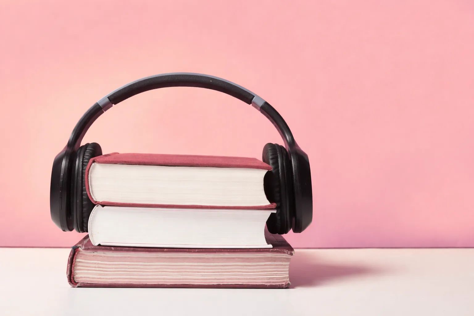 Un casque audio noir posé sur une pile de trois livres reliés, devant un fond rose.