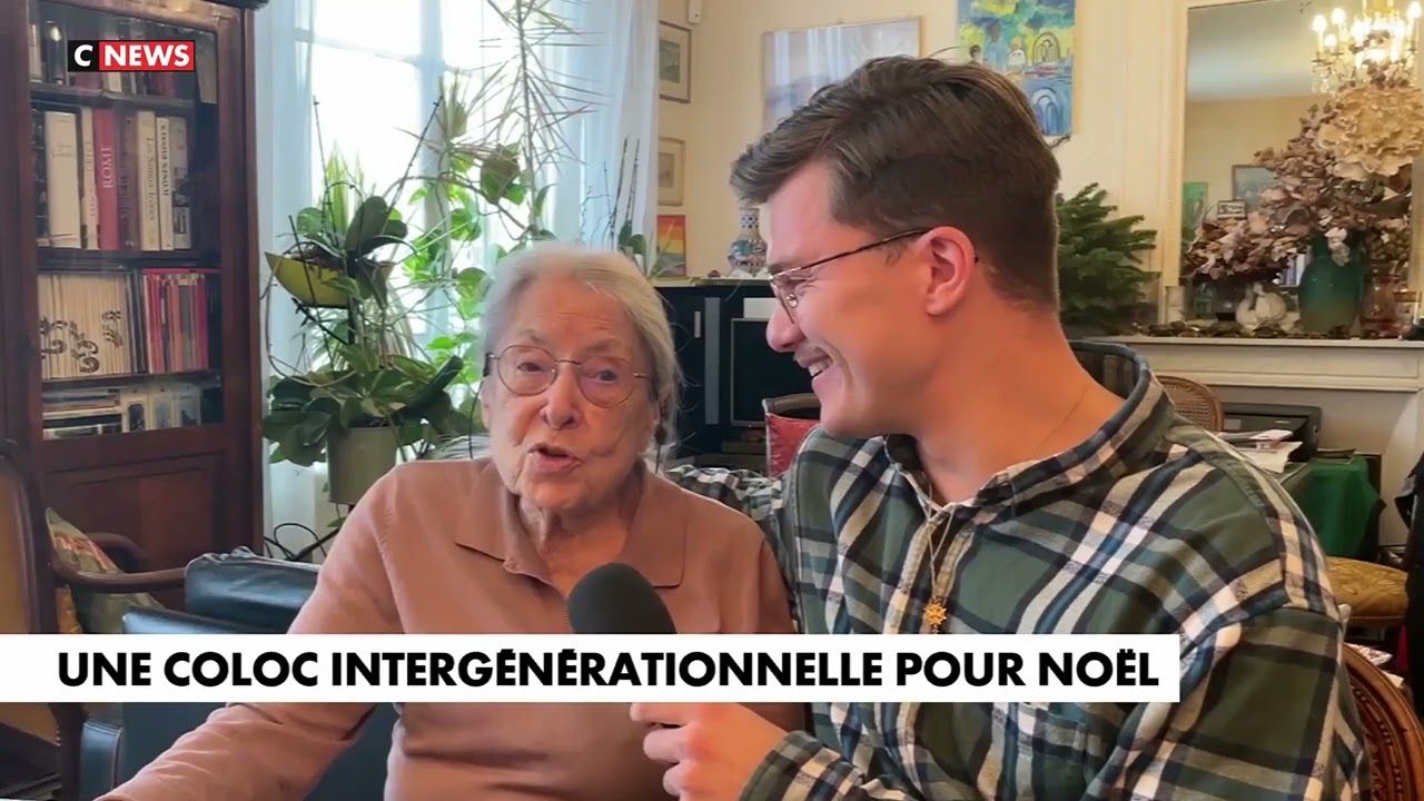 Une hébergeuse âgée et un jeune homme souriant, assis côte à côte dans un salon, répondent à un journaliste.